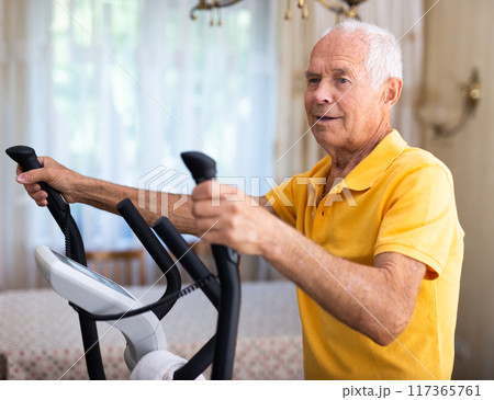 Fit senior man at home doing cardio work out on an elliptical machine 117365761