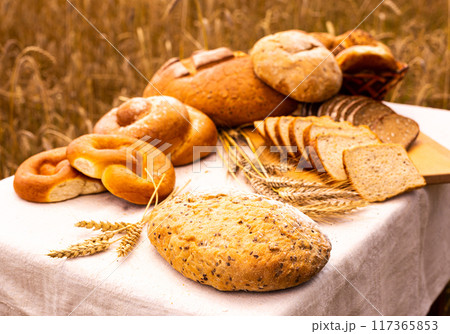 Piece of fresh bread on table against background of grain field 117365853