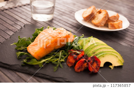 Baked sea trout fillet with fresh vegetables and herbs on black board 117365857