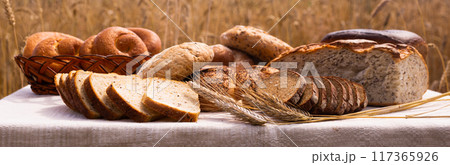 Lot of different flavored bread, wheat, rye, on the table in the field outside 117365926