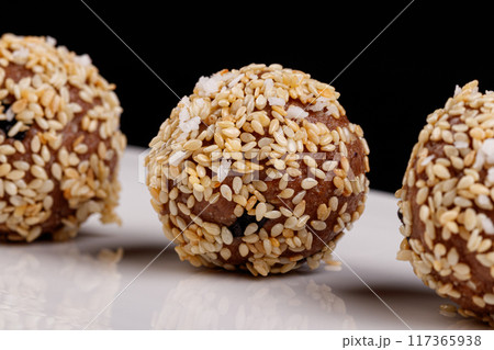 Beautiful candies with sesame seeds on a white plate on a black background Beautiful candies with sesame seeds on a white plate on a black background 117365938