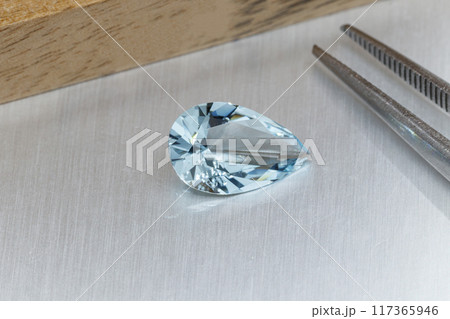 macro mineral faceted stone aquamarine with tweezers on a gray background 117365946