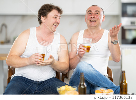 Two adult male friends drinking beer and eating chips at home. Bad habits, eating disorder, alcoholism 117366138