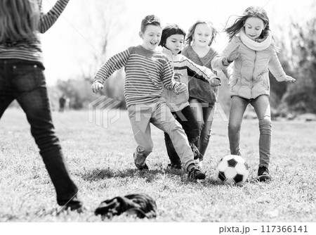 Girls and boy playing soccer in park in autumn Girls and boy playing soccer in park in autumn 117366141