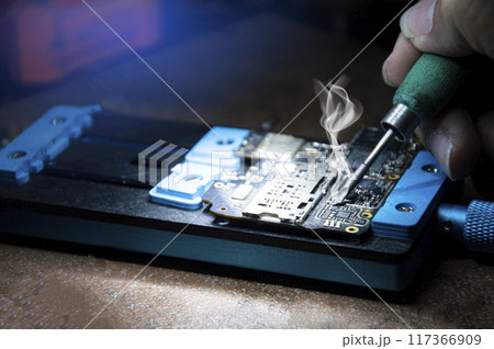 Side view of mechanic doing repairs Smartphone motherboard, smartphone repair, circuit repair Side view of mechanic doing repairs Smartphone motherboard, smartphone repair, circuit repair 117366909