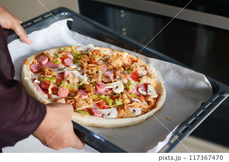 When baking a homemade pizza in the oven, ensure safety by wearing a protective glove on your hand 117367470