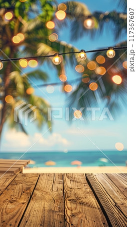 Empty wooden planks table against a blurred background with a sea coast with palm trees and glowing light bulbs in the evening 117367607