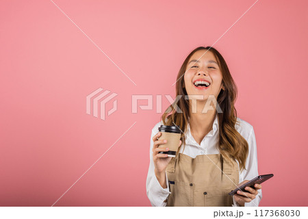 Portrait Asian happy young woman barista bar tender coffee maker holding coffee tea hot cup and mobile phone studio shot isolated on pink background, female smiling hold takeaways cup and smartphone Portrait Asian happy young woman barista bar tender coffee maker holding coffee tea hot cup and mobile phone studio shot isolated on pink background, female smiling hold takeaways cup and smartphone 117368030