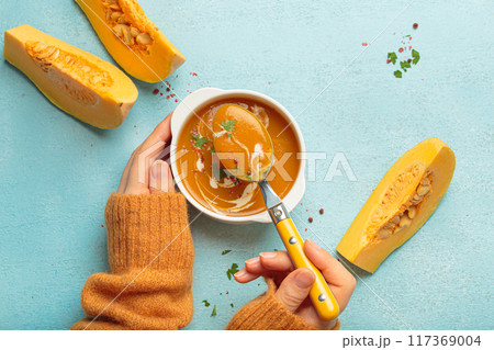 Woman holding spoon eating butternut squash soup with cream on blue background top view 117369004