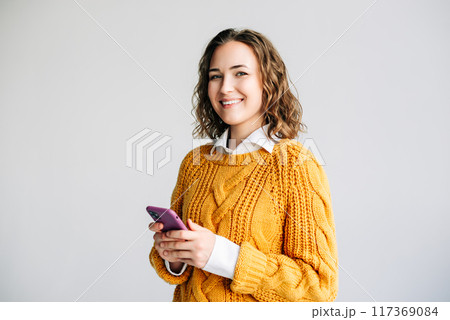 Happy Woman Using Smartphone. Smiling young woman with curly hair using her smartphone. She is Happy Woman Using Smartphone. Smiling young woman with curly hair using her smartphone. She is 117369084