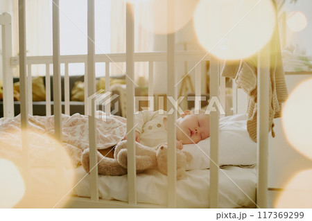 Peacefully sleeping baby boy resting in crib cuddling with stuffed animal surrounded by gentle warm light filters creating a serene atmosphere 117369299