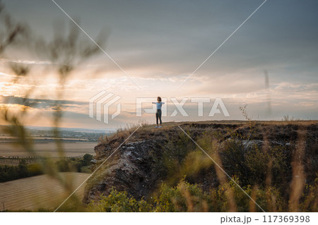 Experiencing a sense of tranquility and peace while gazing at the sunset from the edge of a cliff 117369398