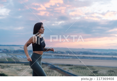 A woman jogging outside at sunset, in a scenic setting, committed to an active lifestyle 117369408