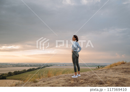 A woman peacefully enjoys a scenic sunset on a hilltop, embracing nature and finding solitude 117369410