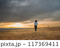 A person is running in an open field during sunset with dramatic clouds in the sky 117369411