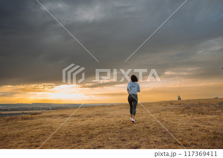 A person is running in an open field during sunset with dramatic clouds in the sky 117369411