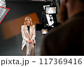 A professional woman wearing a business suit is being filmed in a studio setting 117369416