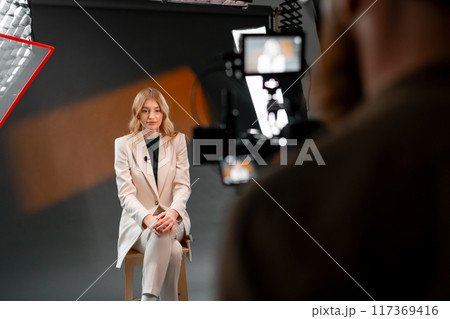 A professional woman wearing a business suit is being filmed in a studio setting 117369416
