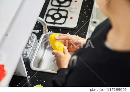 A girl washes vegetables in a toy kitchen. Plastic toys for small children. Children play and cook at home or in kindergarten. Kids play with a stove, dishes, sink, vegetables. High quality photo 117369695