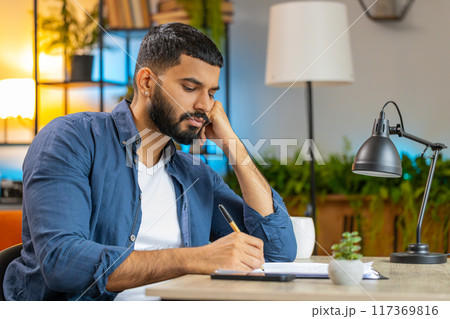 Indian man freelancer working with documents from home office analyzing reading business report 117369816