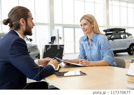 Woman buying new automobile completes purchase with male seller in car showroom Woman buying new automobile completes purchase with male seller in car showroom 117370677