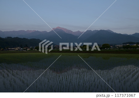 北杜市白州町、田植えの済んだ田んぼに朝焼けの南アルプス甲斐駒ケ岳が姿を落とす 117371067