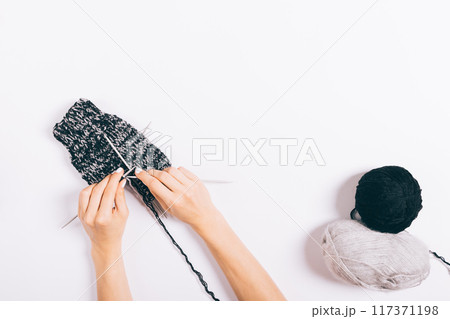 A person is knitting a hat with a black and white pattern 117371198