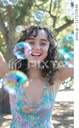 Cheerful woman twirling surrounded by colorful bubbles in sunny outdoor environment 117372640