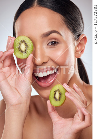 Kiwi makes for a nourishing booster to your skincare routine. Studio portrait of a beautiful young woman posing with kiwi against a grey background. Kiwi makes for a nourishing booster to your skincare routine. Studio portrait of a beautiful young woman posing with kiwi against a grey background. 117372881