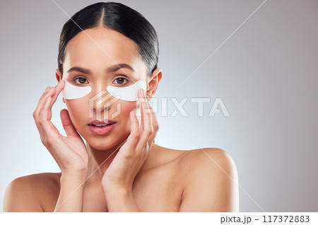 Giving her eyes a surge of moisture. Studio portrait of a beautiful young woman wearing under-eye patches against a grey background. Giving her eyes a surge of moisture. Studio portrait of a beautiful young woman wearing under-eye patches against a grey background. 117372883