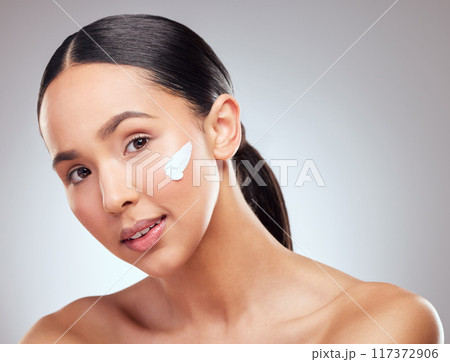 Moisturising helps your skin stay young. Studio portrait of a beautiful young woman applying moisturiser to her face against a grey background. 117372906