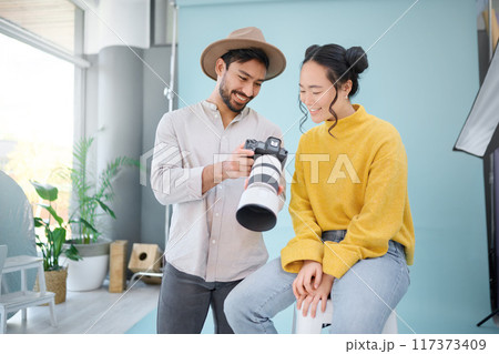 Creative, photographer and model choosing a picture on the camera from the photoshoot in the studio. Photography, creativity and cameraman talking to a woman for the best image on a artistic set. 117373409