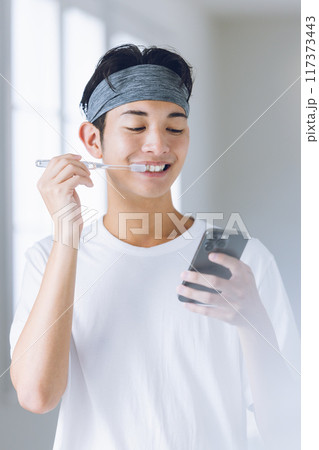 スマホを見ながら歯磨きをする若い男性 117373443