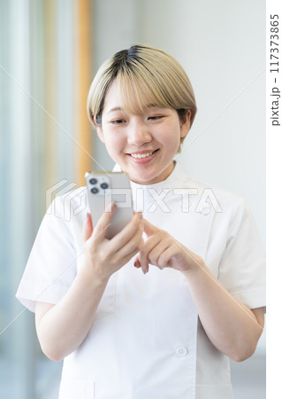 スマホを持つ金髪ショートヘアの若い女性整体師(髪色自由、自分らしく働く、職場環境) スマホを持つ金髪ショートヘアの若い女性整体師(髪色自由、自分らしく働く、職場環境) 117373865