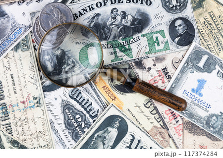 Old west US banknotes and silver certificates with silver dollar coins and magnifying glass Old west US banknotes and silver certificates with silver dollar coins and magnifying glass 117374284