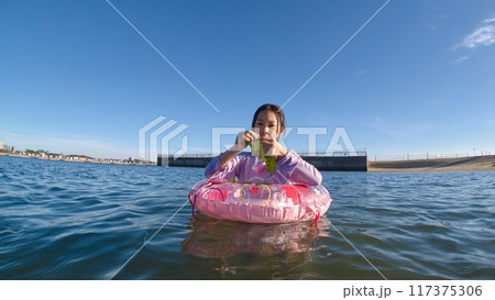 真夏の海水浴場で浮き輪を使って水遊びする小学生の女の子の様子 117375306