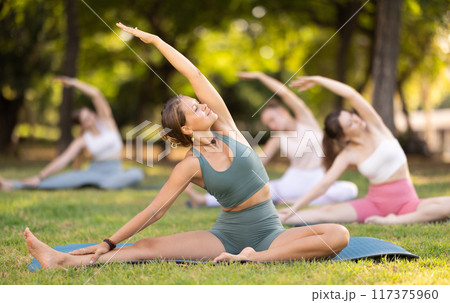 Yoga lesson visitors girls perform Parivritta Janu Shirshasana in park Yoga lesson visitors girls perform Parivritta Janu Shirshasana in park 117375960