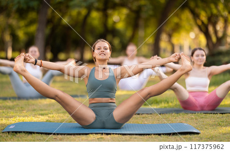 Girls practicing hatha yoga in summer garden, stretching in an asymmetrical seated asana Parivritta Janu Sirsasana with a forward bend and an outstretched arm 117375962