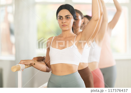 Young girl practicing third arm position holding by ballet barre Young girl practicing third arm position holding by ballet barre 117376437