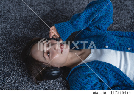 カーペットに寝転んで音楽に浸るミドルの女性 117376459