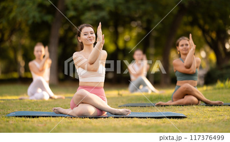 Yoga training in summer sunny park - girls in kagasana pose on mats Yoga training in summer sunny park - girls in kagasana pose on mats 117376499