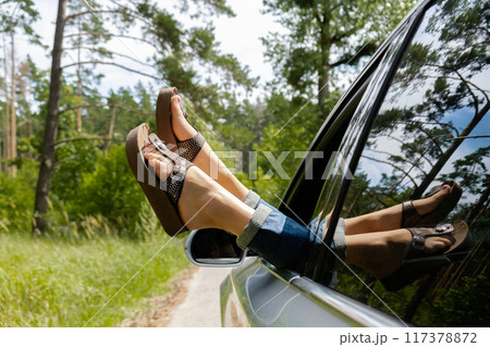 Female legs in blue jeans out of car window. Concept of comfortable local travel vacation holiday. Reduce carbon footprint. Woman resting in road trip  117378872