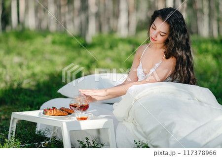 Young woman has breakfast in bed in a summer forest 117378966