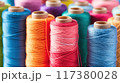 Close-up view of various colorful spools of thread arranged vertically, showcasing vibrant shades and textures for sewing projects.. 117380028