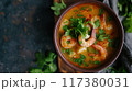 A flavorful bowl of spicy shrimp soup garnished with fresh cilantro and chili peppers, served with lime wedges on the side.. 117380031