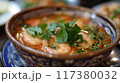 A flavorful bowl of spicy shrimp soup garnished with fresh cilantro and chili peppers, served with lime wedges on the side.. 117380032