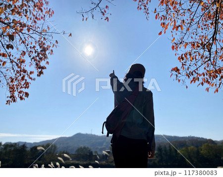 紅葉の中で太陽を指さす女性の後ろ姿 紅葉の中で太陽を指さす女性の後ろ姿 117380083