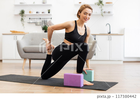 Woman practicing yoga at home with blocks in bright living room Woman practicing yoga at home with blocks in bright living room 117380442