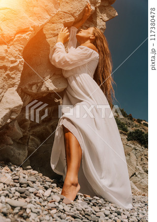 Woman summer travel sea. Happy lady with long hair in white dress enjoy taking photo outdoors for memories. Woman traveler posing on beach at sea surrounded by volcanic mountains, sharing emotions Woman summer travel sea. Happy lady with long hair in white dress enjoy taking photo outdoors for memories. Woman traveler posing on beach at sea surrounded by volcanic mountains, sharing emotions 117380478