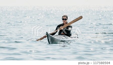 Woman sea kayak. Happy smiling woman in kayak on ocean, paddling with wooden oar. Calm sea water and horizon in background. Active lifestyle at sea. Summer vacation. 117380504